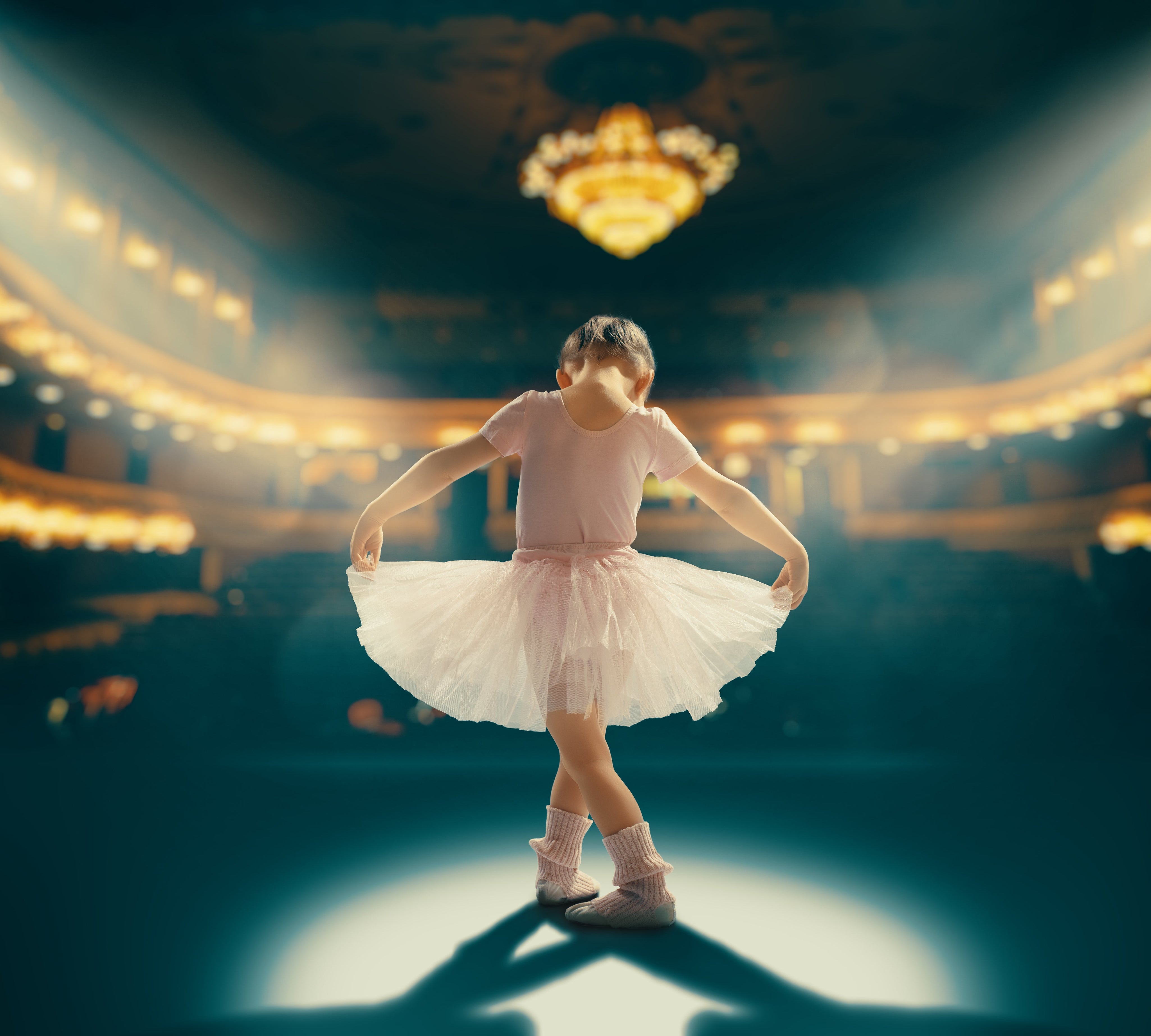 Dance Recitals: Young ballerina in pink leotard and white tutu standing in spotlight on stage, performing with elegant theater backdrop and chandelier